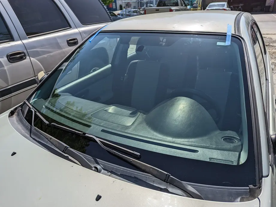 A freshly installed windshield on a silver sedan with blue retention tape at the top edge