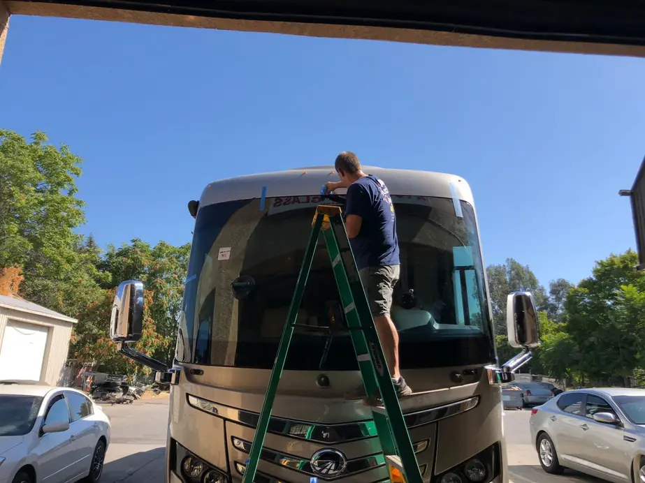 Installer on a ladder setting a motorhome windshield in the Oroville lot