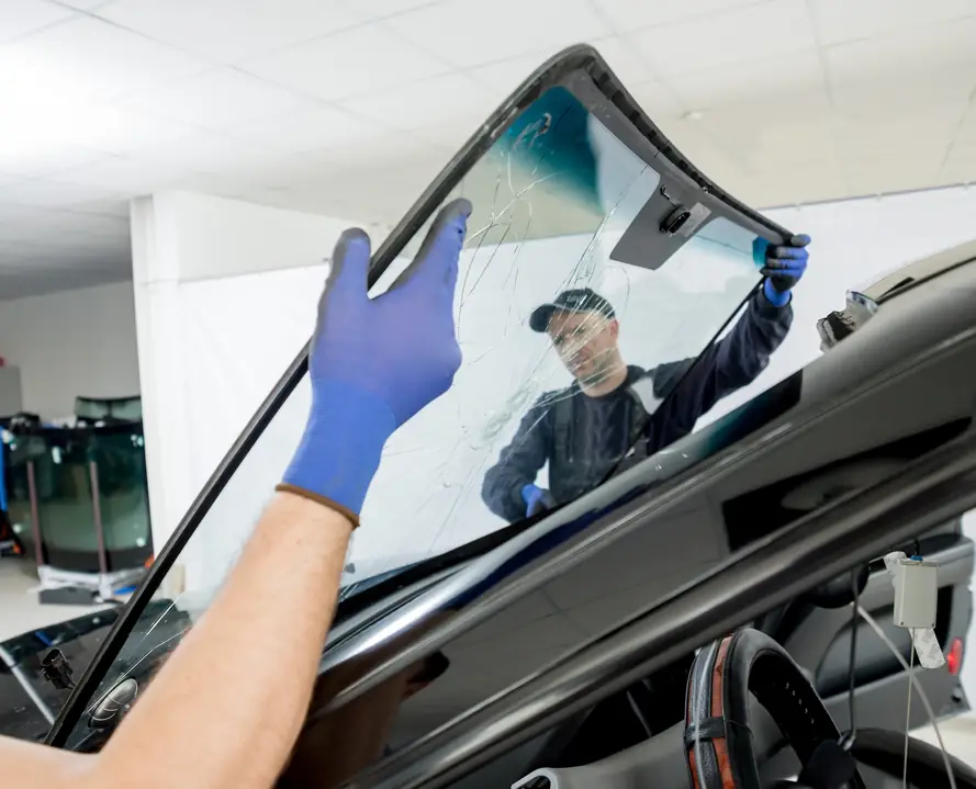 Technician lifting a new windshield into place in the shop